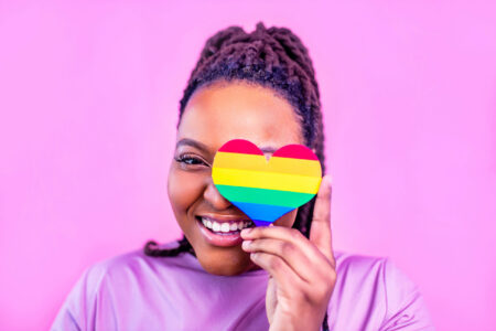 afro american woman holding a heart shape in pink studio background